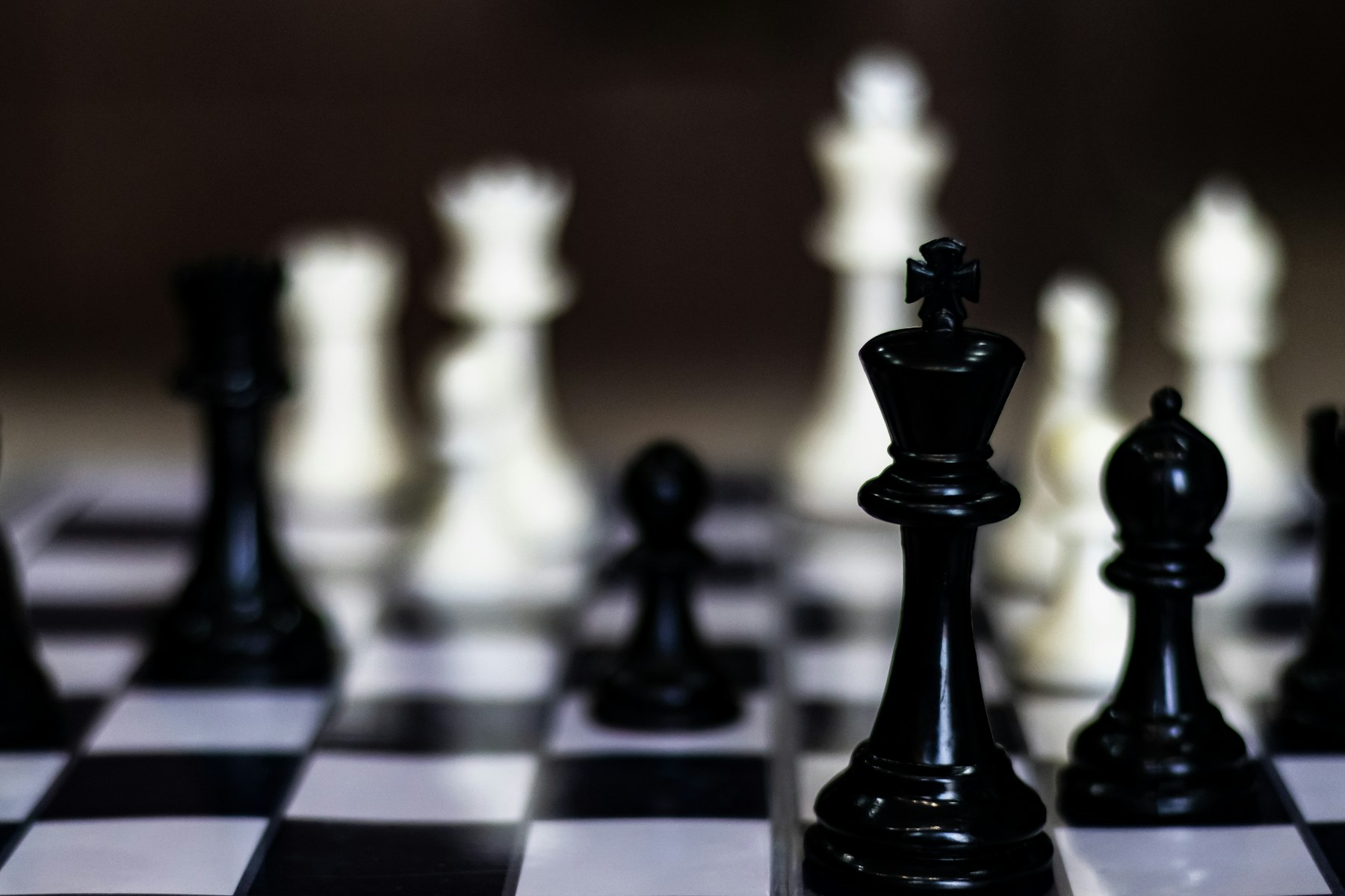 A black king chess piece in sharp focus on a chessboard, with the opposing pieces blurred behind — strategic judgement under uncertainty.